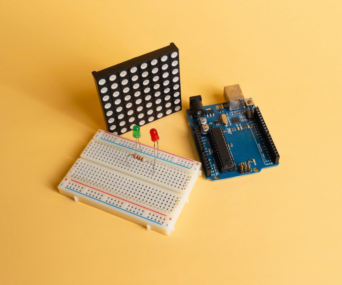 Electronic components including a breadboard, LED, and circuit board on a yellow background