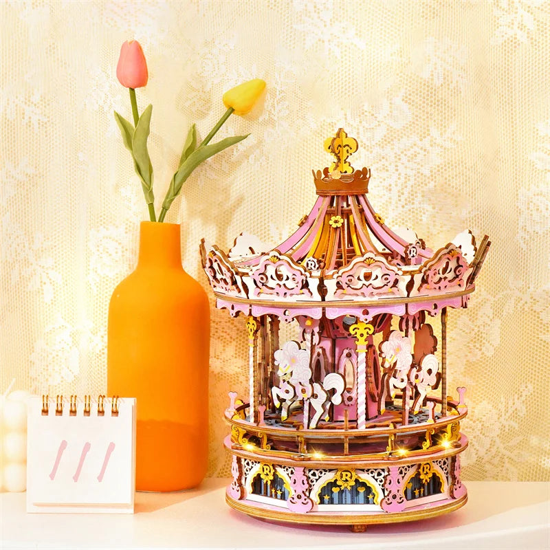 Decorative carousel with horses on a table next to an orange vase with flowers and a white notebook.