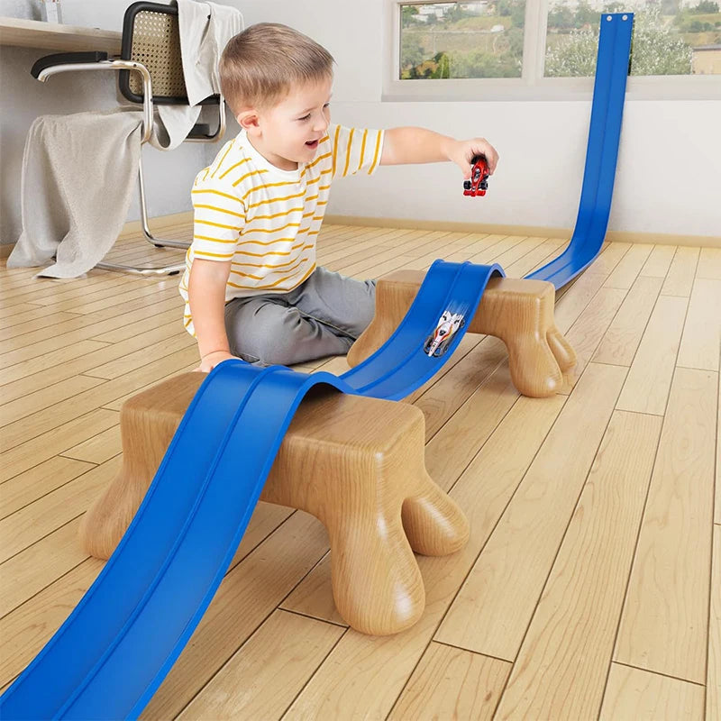 Child playing with a toy car on a blue track set on a wooden floor.