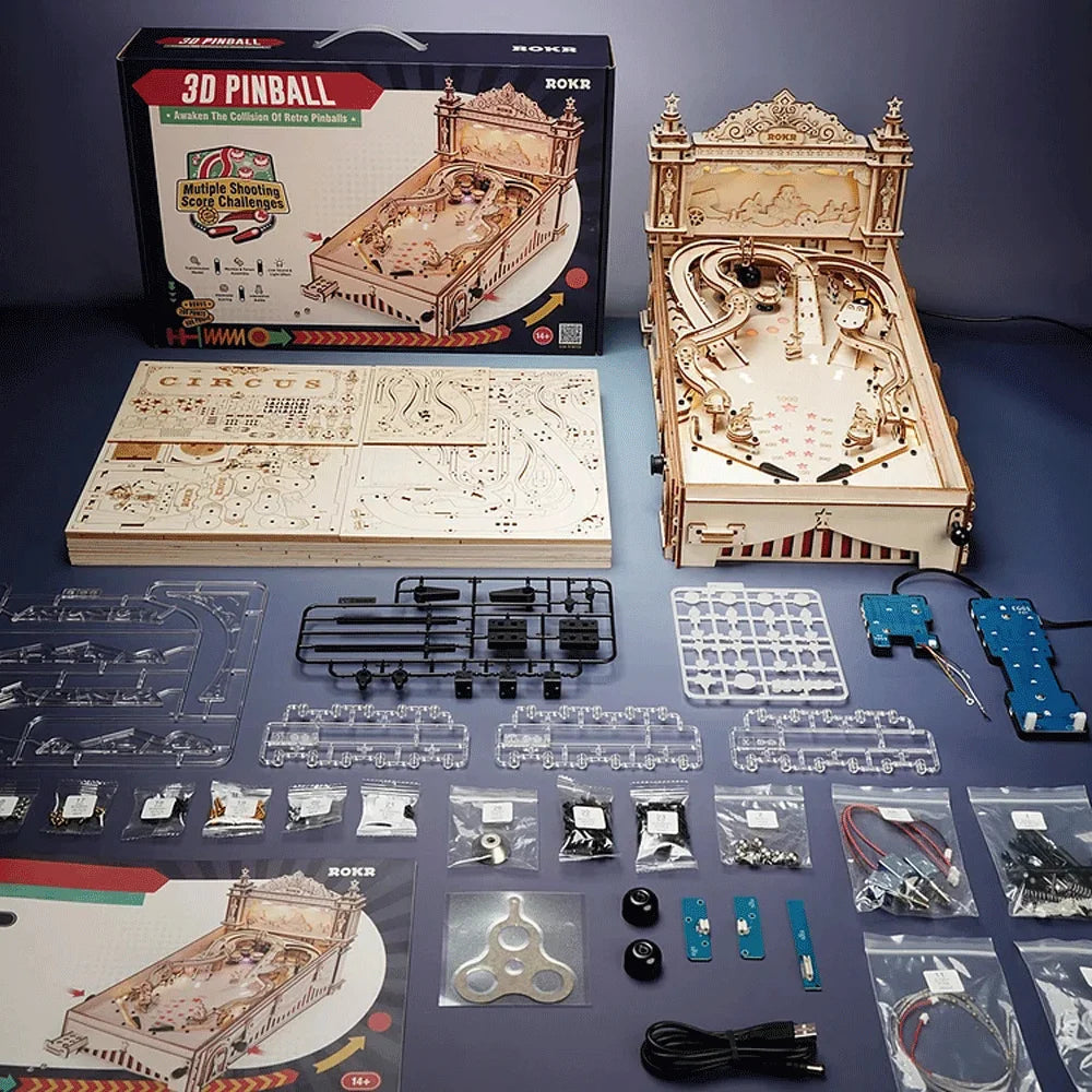 Wooden 3D pinball machine kit with components and packaging on a blue surface