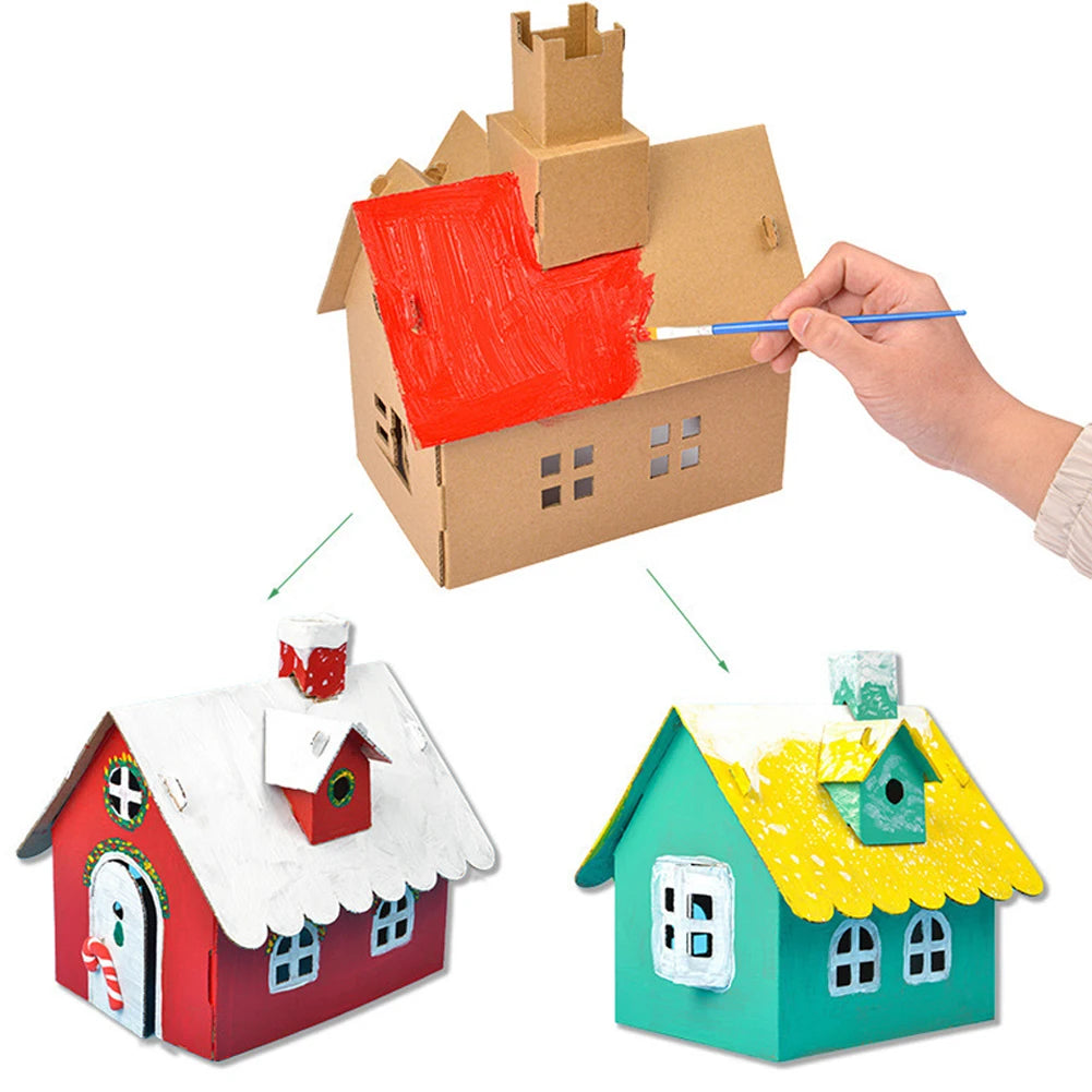 Cardboard house model with colorful roofs being painted, and a hand holding a paintbrush.