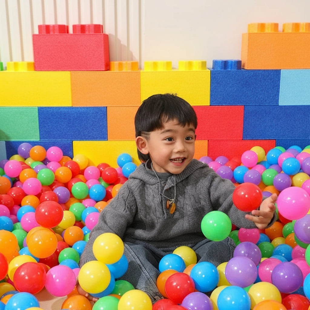 Child playing with colorful balls in a ball pit surrounded by foam blocks.