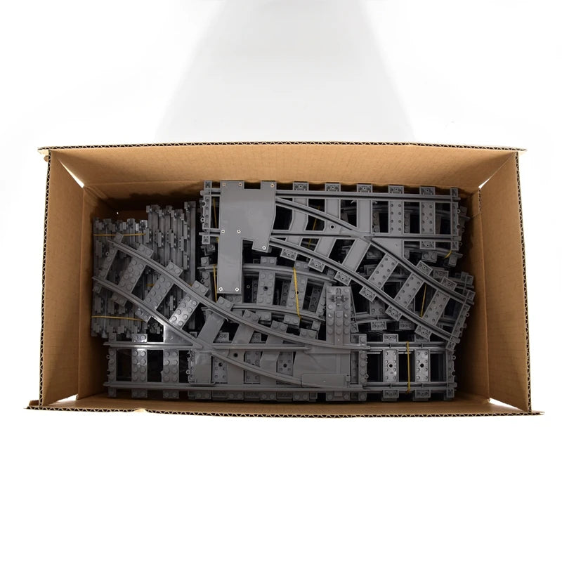 Cardboard box with gray toy train tracks inside on a white background