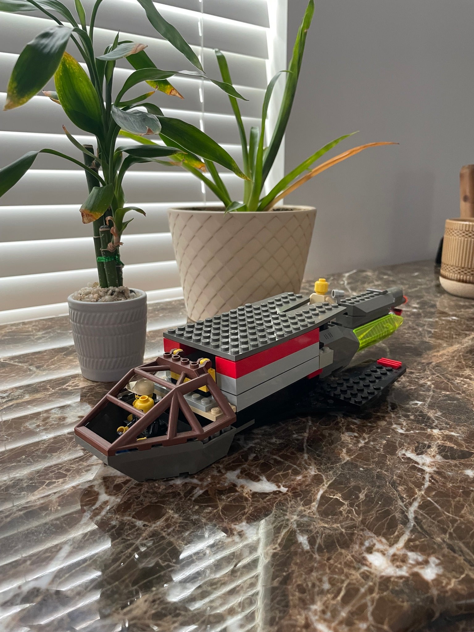 Toy spaceship made of interlocking bricks on a marble surface with plants in the background